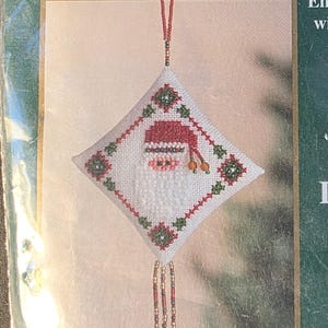 May include: A Mill Hill Tiny Treasured Diamond embellished cross stitch kit titled Diamond Ho Ho. The packaging features a diamond-shaped ornament with a Santa Claus design, red and green accents, and beaded tassels. Finished size is 3.25 inches by 5.75 inches.