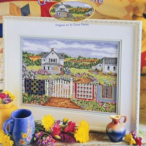 May include: A framed cross-stitch artwork titled "Quilts for Sale" by Diane Phalen. The artwork depicts a rural scene with a white house, a picket fence, and quilts hanging outside. The frame size is 18.5" x 14.5", and the design size is 9.5" x 13.5".