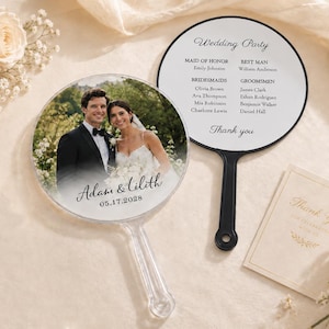 Puede incluir: Dos abanicos de boda redondos con mangos negros. Uno muestra una fotografía de una pareja con el texto Adam & Lilith 05.17.2028. El otro muestra una lista de la corte nupcial con Maid of Honor, Best Man, Bridesmaids y Groomsmen.