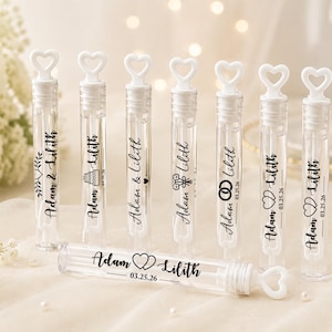 May include: A set of clear plastic bubble wands with white heart-shaped caps. Each wand features black printed text reading Adam & Lilith and the date 03.25.26, accompanied by various small icons including a wedding cake, flowers, and interlocking rings.