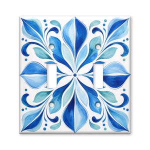 May include: A double light switch wall plate featuring a symmetrical watercolor-style floral pattern in shades of navy, royal blue, and light cyan on a white background, with two rectangular cutouts for switches and four screw holes.