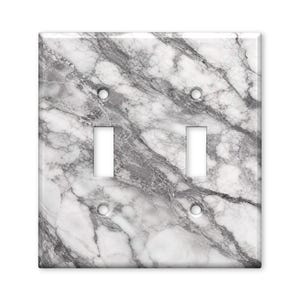 May include: A double light switch wall plate featuring a white and gray marble pattern with realistic veining. The rectangular cover includes two vertical rectangular cutouts for switches and four circular screw holes at the corners.