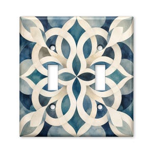 May include: A double light switch wall plate featuring a symmetrical, interlocking geometric pattern in shades of deep navy blue, soft teal, and creamy off-white. The design has a watercolor texture with two rectangular cutouts for switches.