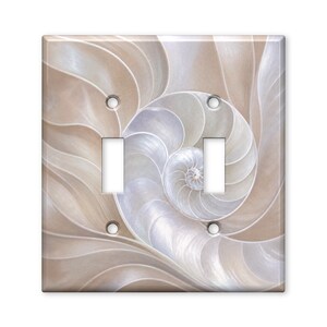 May include: A double light switch wall plate featuring a high-resolution print of a nautilus shell. The design displays a spiral pattern in shades of beige, cream, and soft white, with two rectangular cutouts for switches and four screw holes.