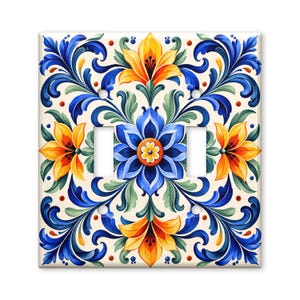 May include: A double light switch wall plate featuring a symmetrical floral pattern with vibrant yellow, blue, and green colors on a cream background. The design includes stylized petals and scrolling leaves arranged in a repeating decorative motif.