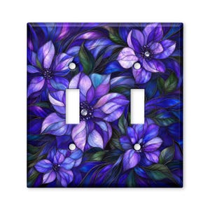 May include: A double light switch wall plate featuring a stained glass style pattern of vibrant purple and blue flowers with dark green leaves. The rectangular cover has two vertical rectangular cutouts for switches and three circular screw holes.
