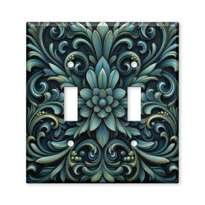 May include: A double light switch wall plate featuring a symmetrical teal and dark blue floral scrollwork pattern. The design includes a central flower motif surrounded by intricate, curved leaf-like shapes and small circular accents.