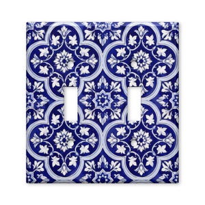 May include: A double light switch wall plate featuring a repeating pattern of white floral and geometric motifs set against a deep blue background. The rectangular cover includes two vertical rectangular cutouts for switches and four screw holes.
