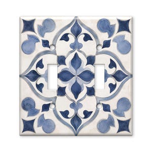 May include: A square double light switch wall plate featuring a symmetrical watercolor pattern in shades of navy blue, light blue, and white. The design consists of intricate floral and geometric motifs with four screw holes and two rectangular cutouts.