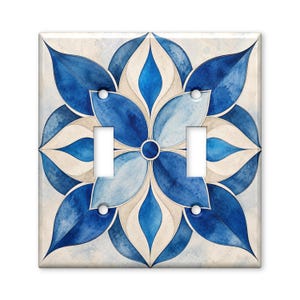 May include: A square double light switch wall plate featuring a symmetrical floral mandala pattern in shades of deep navy, royal blue, and light sky blue against a cream-colored background with a subtle watercolor texture and four screw holes.