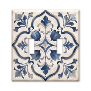 May include: A square double light switch wall plate featuring a symmetrical watercolor-style pattern in shades of navy blue, light blue, and beige. The design consists of intricate floral and scrollwork motifs centered on a cream background.