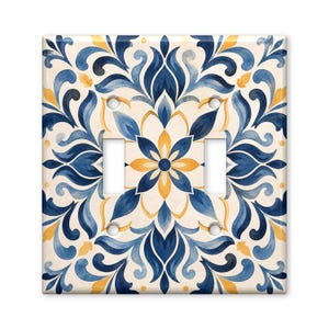 May include: A square double light switch wall plate featuring a symmetrical floral pattern in shades of navy blue, light blue, and golden yellow on an off-white background. The design includes two rectangular cutouts for switches and four screw holes.