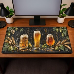 May include: A rectangular desk mat featuring a dark background with three distinct beer glasses filled with golden liquid and foam. The design includes illustrations of green hop cones, wheat stalks, and circular geometric patterns.