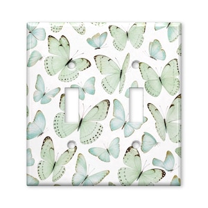 May include: A rectangular double light switch cover plate featuring a repeating pattern of pale mint green and soft blue butterflies on a white background. The plate includes two vertical rectangular cutouts for switches and three screw holes.