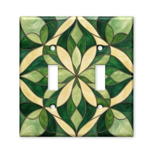 May include: A double light switch wall plate featuring a symmetrical stained glass pattern in shades of emerald green, forest green, and cream. The design consists of interlocking curved shapes and lines, with two rectangular cutouts for switches.