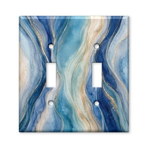 May include: A double toggle light switch plate cover featuring a fluid, marbled pattern in shades of navy blue, light blue, and teal, accented with thin, shimmering gold veins that flow vertically across the rectangular surface.