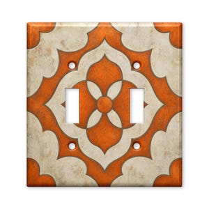 May include: A double light switch wall plate featuring a repeating geometric pattern in burnt orange and off-white. The design consists of interlocking quatrefoil shapes with a distressed, textured finish and four screw holes for mounting.