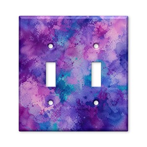 May include: A rectangular double light switch wall plate featuring a vibrant watercolor pattern in shades of purple, violet, and blue. The design includes splatters and blended color washes across the entire surface with two vertical rectangular cutouts.