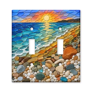 May include: A double light switch cover plate featuring a vibrant mosaic-style print of a beach at sunset. The design displays a bright yellow sun over a blue ocean with white waves crashing onto a shore covered in multicolored smooth pebbles.