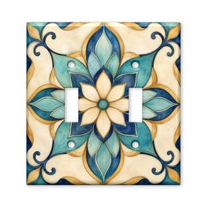May include: A double light switch wall plate featuring a symmetrical floral mandala pattern in shades of cream, teal, dark blue, and gold. The square cover has two rectangular cutouts for switches and four circular holes for mounting screws.