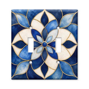 May include: A double light switch wall plate featuring a symmetrical floral mandala pattern in shades of deep navy blue, light blue, and cream. The design is outlined with thin gold lines and includes two rectangular cutouts for switches.