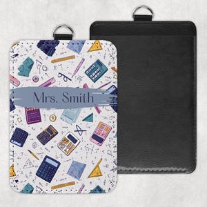 May include: A white and black patterned ID badge holder with a black leather back. The front features a repeating pattern of calculators, protractors, and other school supplies. The name "Mrs. Smith" is printed on a blue banner.