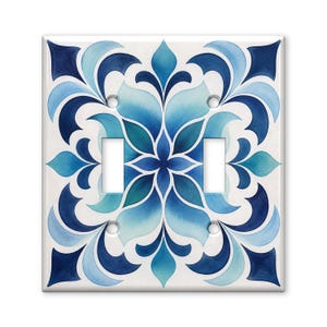 May include: A square double light switch wall plate featuring a symmetrical floral pattern in shades of navy, royal blue, and light turquoise on a white background. The plate has two rectangular cutouts for switches and four screw holes.