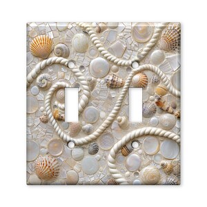 May include: A double light switch wall plate featuring a decorative mosaic pattern of various seashells and white rope accents. The design includes small, smooth, iridescent shell fragments and larger spiral seashells in shades of tan, brown, and white.