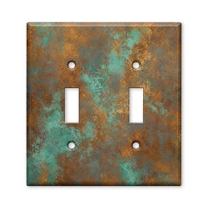 May include: A rectangular double toggle light switch wall plate featuring a weathered, oxidized metal finish with a mottled pattern of deep copper brown and vibrant turquoise green hues, including four screw holes and two vertical switch openings.