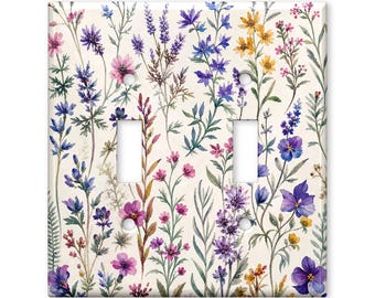 May include: A double light switch wall plate featuring a watercolour print of various wildflowers in shades of purple, pink, blue, and yellow on a cream background. The rectangular plate has two vertical rectangular cutouts for switches.