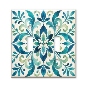 May include: A double light switch wall plate featuring a symmetrical watercolor pattern of swirling leaves and floral motifs in shades of teal, dark blue, and light green on a cream-colored background with four screw holes for installation.