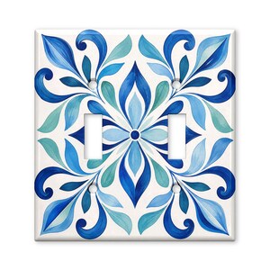 May include: A square double light switch wall plate featuring a symmetrical painted pattern of blue, teal, and white stylized leaves and floral motifs. The design is centered on a white background with two rectangular cutouts for toggle switches.