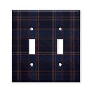 May include: A double light switch wall plate featuring a dark navy blue and copper brown plaid pattern. The rectangular cover includes two vertical rectangular cutouts for switches and four circular screw holes positioned at the corners.