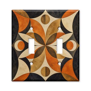 May include: A double light switch wall plate featuring a symmetrical geometric pattern of interlocking curved shapes in shades of burnt orange, dark charcoal, and cream. The design includes four circular screw holes and two rectangular cutouts.