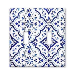 May include: A double light switch wall plate featuring a repeating blue and white floral pattern. The design consists of symmetrical, interconnected geometric shapes with intricate blue botanical motifs on a crisp white background, including two rectangular cutouts for toggle switches and four screw holes.