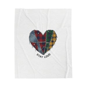 May include: White blanket featuring a heart-shaped design composed of patchwork fabric in various colors, including red, blue, green, and yellow. The heart is stitched together with visible thread and safety pins. The words "STAY LOUD" are printed below the heart.