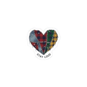 May include: A heart-shaped sticker with a patchwork design. The patches are various colors and patterns, including red plaid, green and yellow plaid, and gray. The patches are sewn together with white stitching and safety pins. The text "STAY LOUD" is at the bottom.