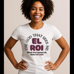 以下が含まれることがあります： 「THE GOD THAT SEES ME EL ROI」の文字が円形にデザインされた白いTシャツ。下には「What God cannot do does not exist」の文字。黒い巻き毛の人がTシャツを着ています。