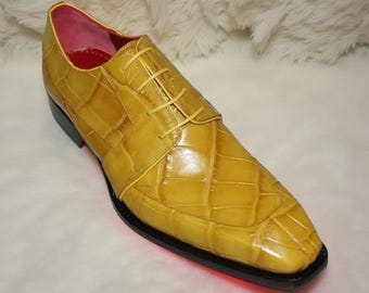 May include: A single yellow leather dress shoe with a textured, crocodile-like pattern. The shoe has a square toe, a black sole, and yellow laces. The interior is pink.