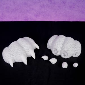 May include: Two white, three-dimensional paw-shaped structures with a porous, mesh-like texture and smooth, pointed claw attachments. Four additional individual smooth white claw pieces are arranged separately between the two paw forms.