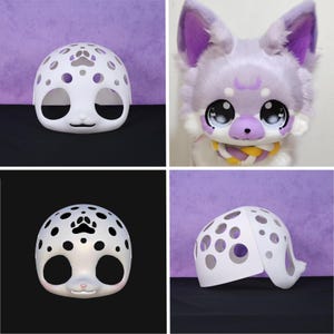 May include: A white, spotted fursuit head base with large eye openings and a small nose. The base has a rounded shape with a paw print design on top. A finished fursuit head with purple accents is also shown.