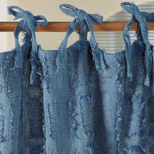 Puede incluir: Cortinas azules con efecto denim con cierres superiores anudados. Las cortinas están hechas de una tela texturizada con bordes deshilachados y cuelgan de una barra de madera. Los cierres superiores están anudados en lazos.