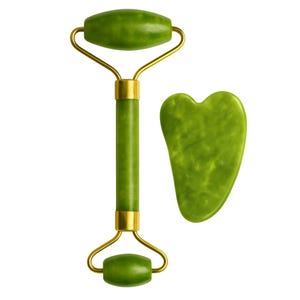 Op de afbeelding: Een groene jade gezichtsroller met goudkleurige metalen accenten en een bijpassende hartvormige gua sha tool. De roller heeft twee jaden stenen en een centrale handgreep. De gua sha tool is glad en gebogen.