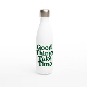 Puede incluir: Botella de agua aislada blanca con tapa plateada. La botella tiene el texto "Good Things Take Time" impreso en verde. La botella está diseñada para mantener las bebidas frías o calientes.