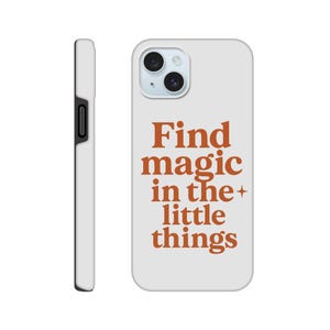 Puede incluir: Funda de teléfono blanca con la frase "Find magic in the little things" en letras naranjas. La funda tiene un recorte para la cámara y un botón lateral negro. La funda está diseñada para un smartphone.