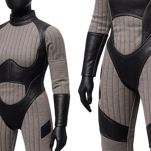 May include: A gray jumpsuit with vertical ribbed texture, featuring black leather-like accents on the bodice, sleeves, and legs. The jumpsuit has a high collar and long sleeves, with black gloves. The design includes padded details.