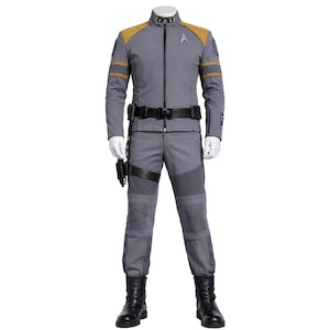 Könnte beinhalten: Ein grauer Starfleet-Anzug mit einer Jacke mit goldenen Schulterakzenten und einem schwarzen Gürtel. Der Anzug umfasst eine passende graue Hose, schwarze Stiefel und ein Holster. Ein Starfleet-Abzeichen ist auf der Jacke zu sehen.