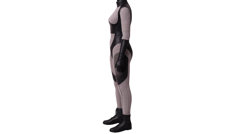 May include: A full-body jumpsuit in shades of gray and black. The suit features a high collar, long sleeves, and a form-fitting design with panels of black material. The outfit is completed with black gloves and boots.