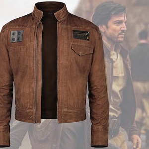 May include: Brown leather jacket with a stand-up collar, two square patches on the left chest, and a small pocket on the right chest. The jacket has a zip closure and a brown shirt underneath.