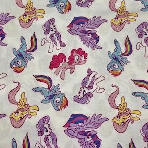 May include: White fabric with a repeating pattern of cartoon ponies in various poses. The ponies are in shades of pink, blue, purple, and yellow, with rainbow manes and wings. A playful design.